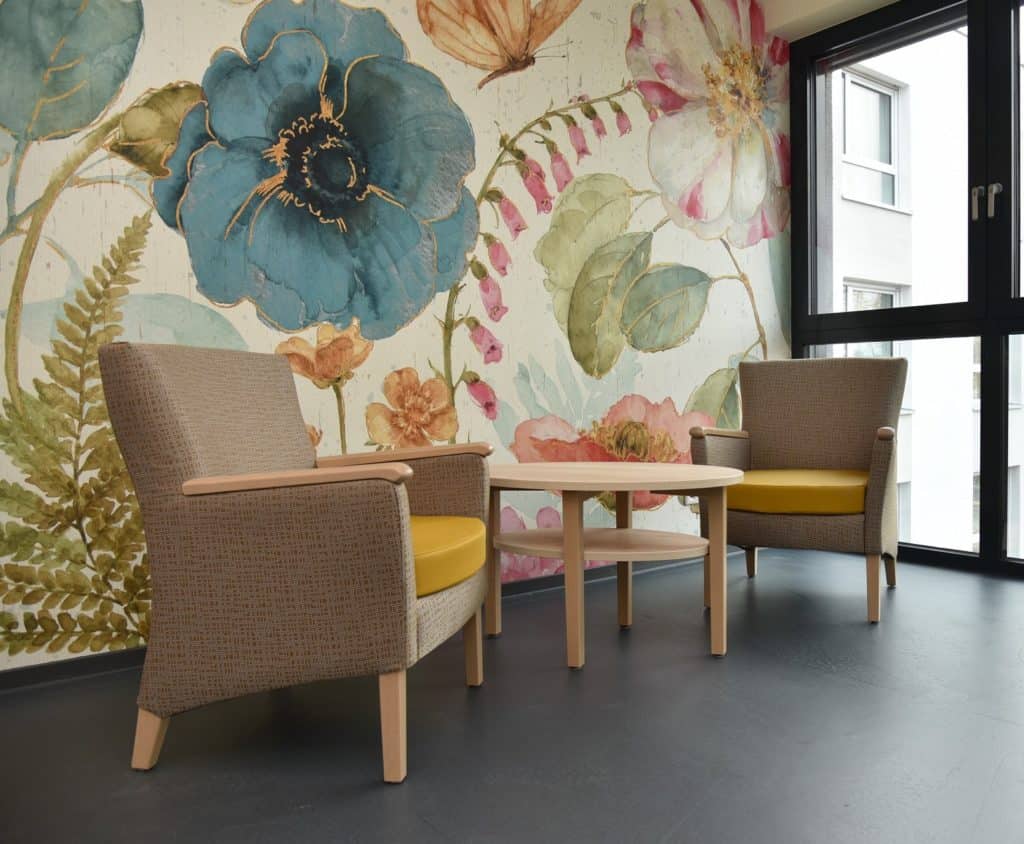 Blick auf eine großblumige Tapete mit rundem Tisch und zwei Sesseln
